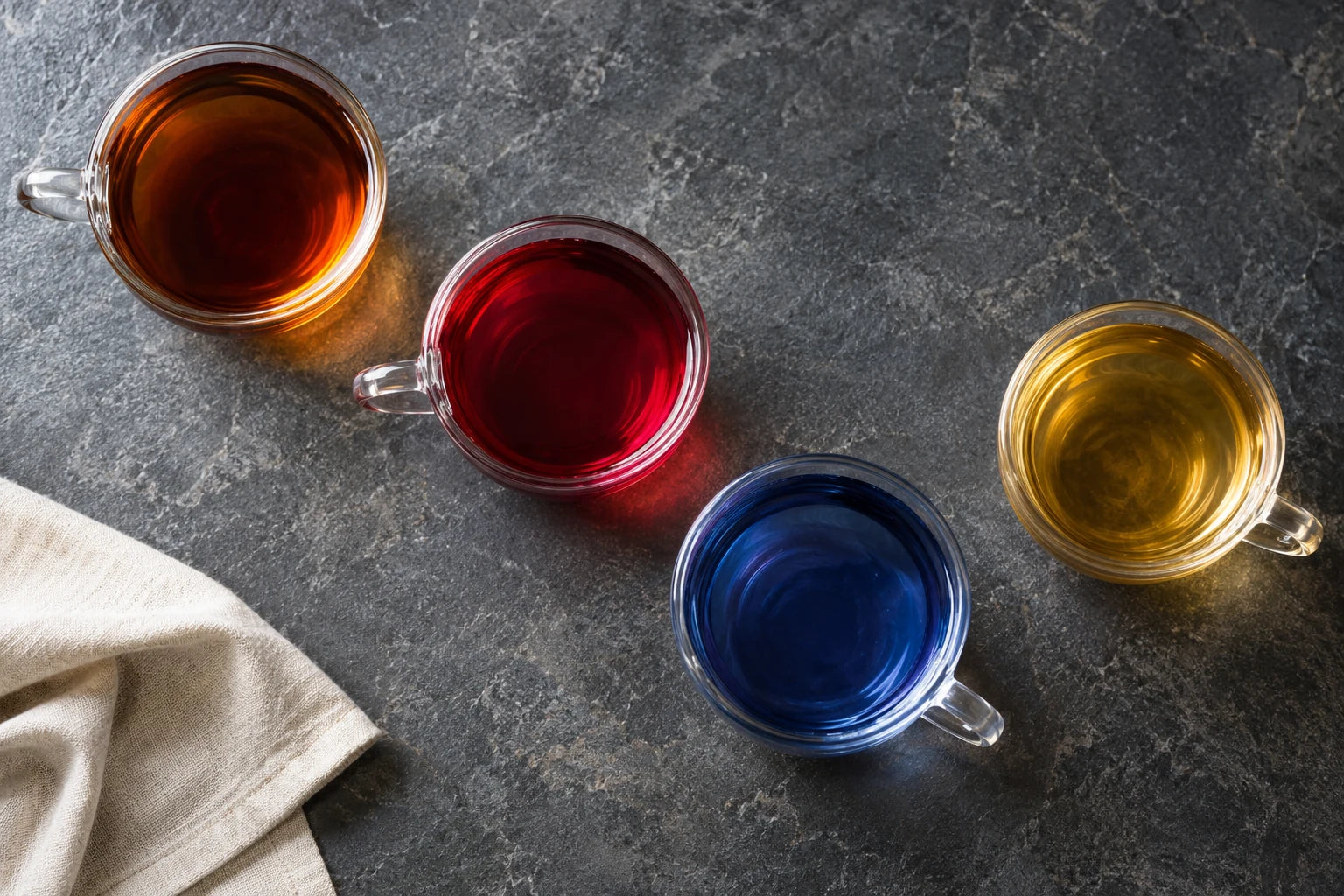 Four glass cups with amber, hibiscus-red, butterfly-pea blue and golden teas